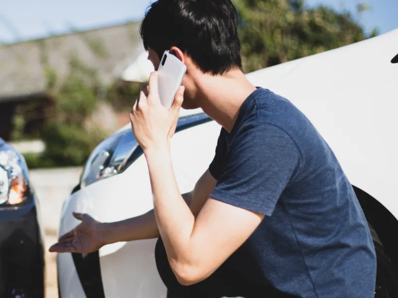 Image showing a car accident with a person talking on the phone with their insurance company. 