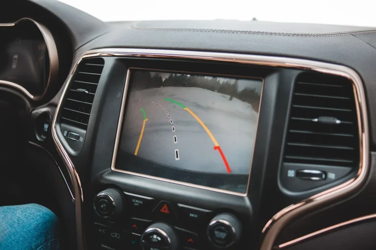 Car dashboard display showing a rearview camera feed with colored parking guidance lines.