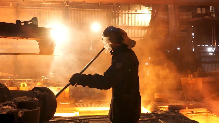 Worker wearing a face shield beside industrial equipment in a factory